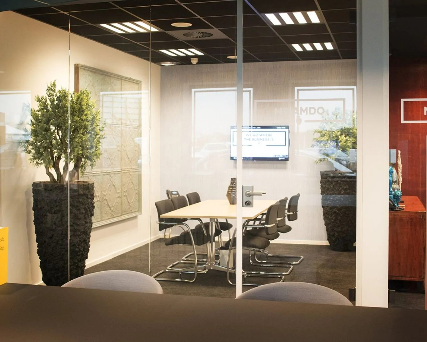 Vergaderruimte met glazen wanden, moderne stoelen, een lange tafel en een scherm aan de muur.