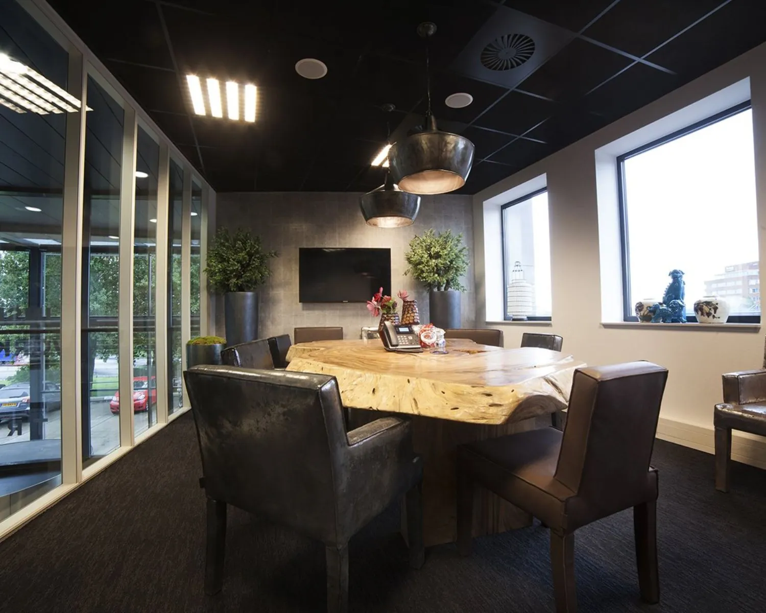 Stijlvol ingerichte vergaderruimte met een robuuste houten tafel, leren stoelen en grote ramen met uitzicht op de stad.