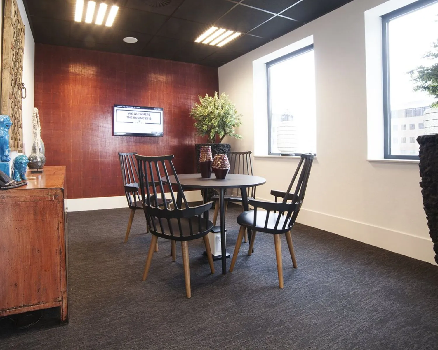 Moderne vergaderruimte met ronde tafel, vier zwarte stoelen, decoratieve planten en een wand met flatscreen.