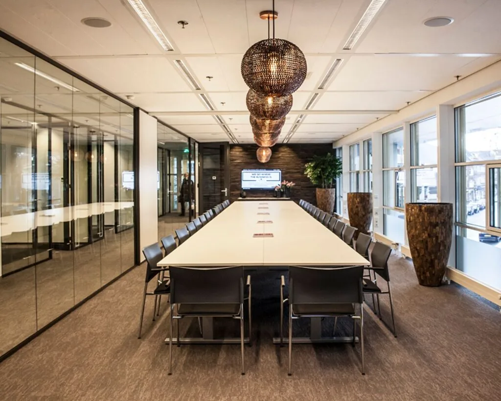 Luxe vergaderruimte met lange tafel, moderne verlichting en grote ramen.