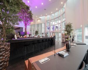 Moderne en open ontvangstruimte met een lange zwarte bar, hoge glazen ramen en sfeerverlichting in paars.