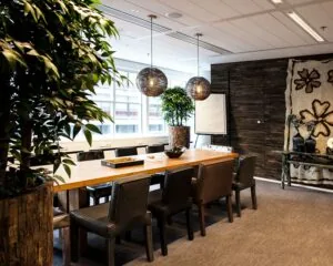 Vergaderruimte met houten tafel, leren stoelen, grote planten en decoratieve verlichting in een moderne, natuurlijke stijl.