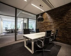 Moderne vergaderruimte met glazen wanden, een witte tafel en zwarte bureaustoelen in een kantooromgeving.