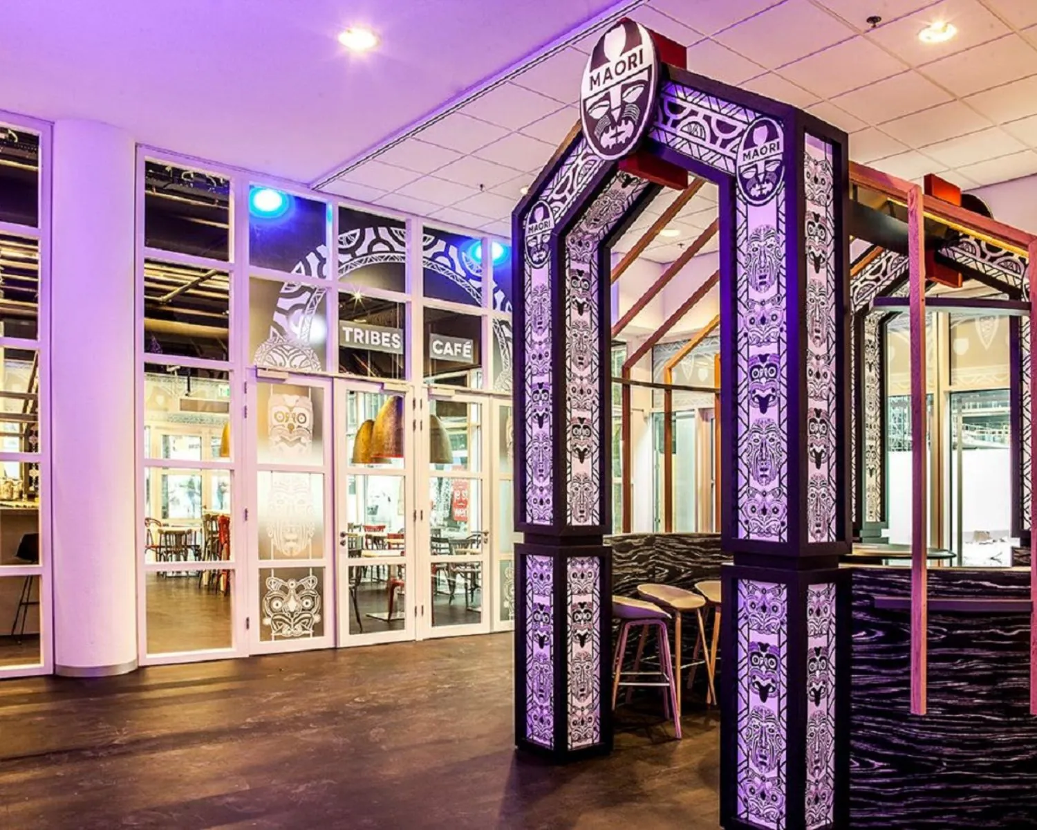 Modern café-interieur met Māori-inspiratie, gedecoreerd met traditionele patronen en het bord "Tribes Café" bij de ingang.