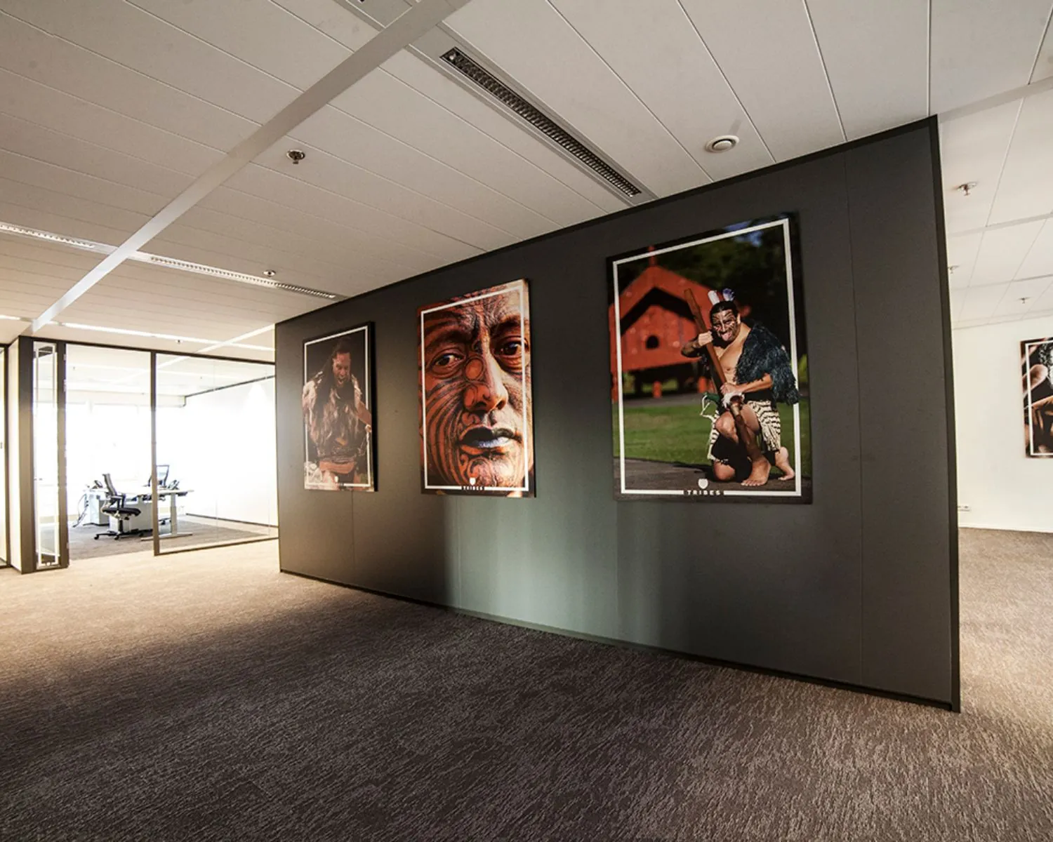 Kantoorruimte met moderne inrichting en een wand met drie grote portretten van Maori-krijgers.