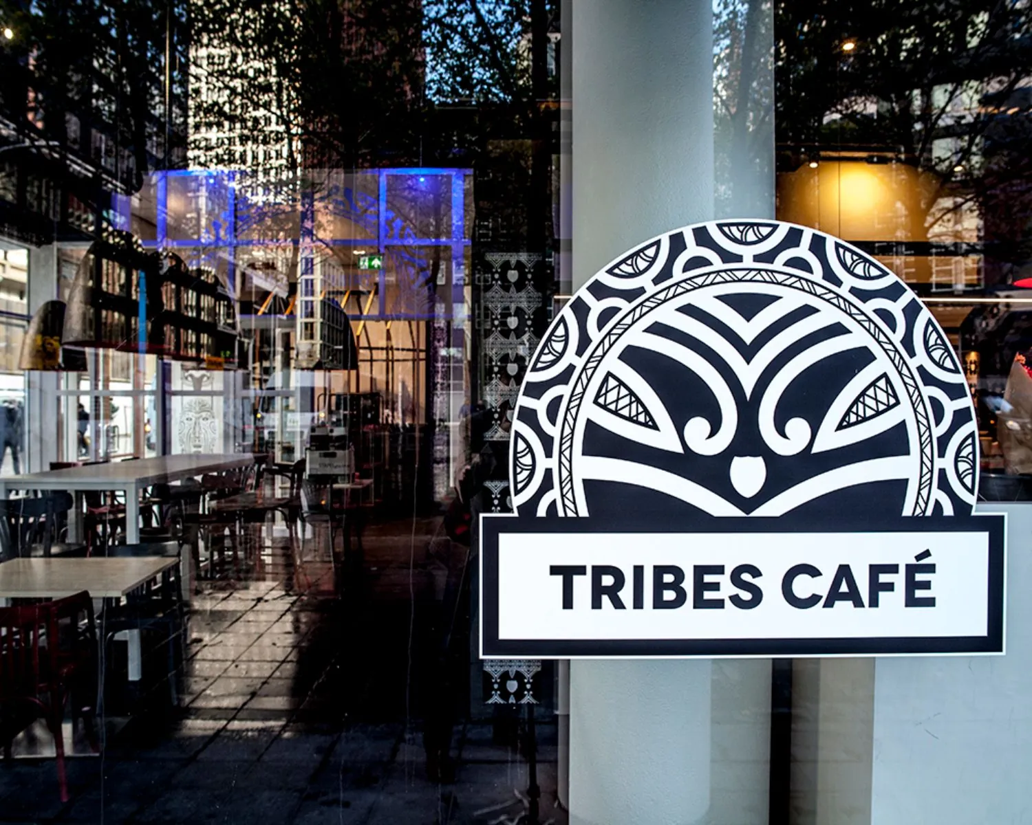 De ingang van Tribes Café met een prominent zwart-wit logo op het raam en zicht op het interieur.