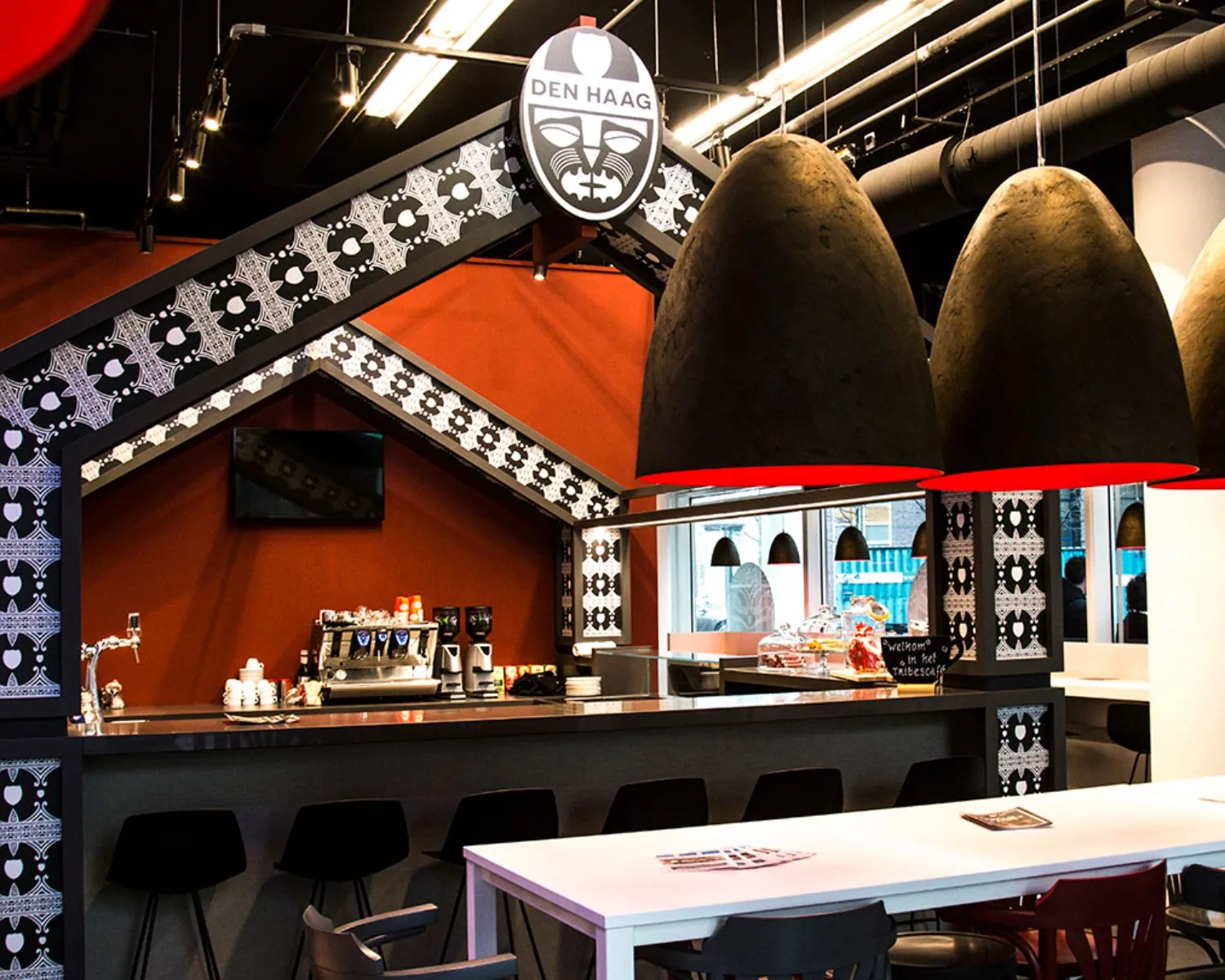 Modern ingerichte koffiebar met opvallende zwarte en witte patronen, grote hanglampen en een Den Haag-logo boven de bar.
