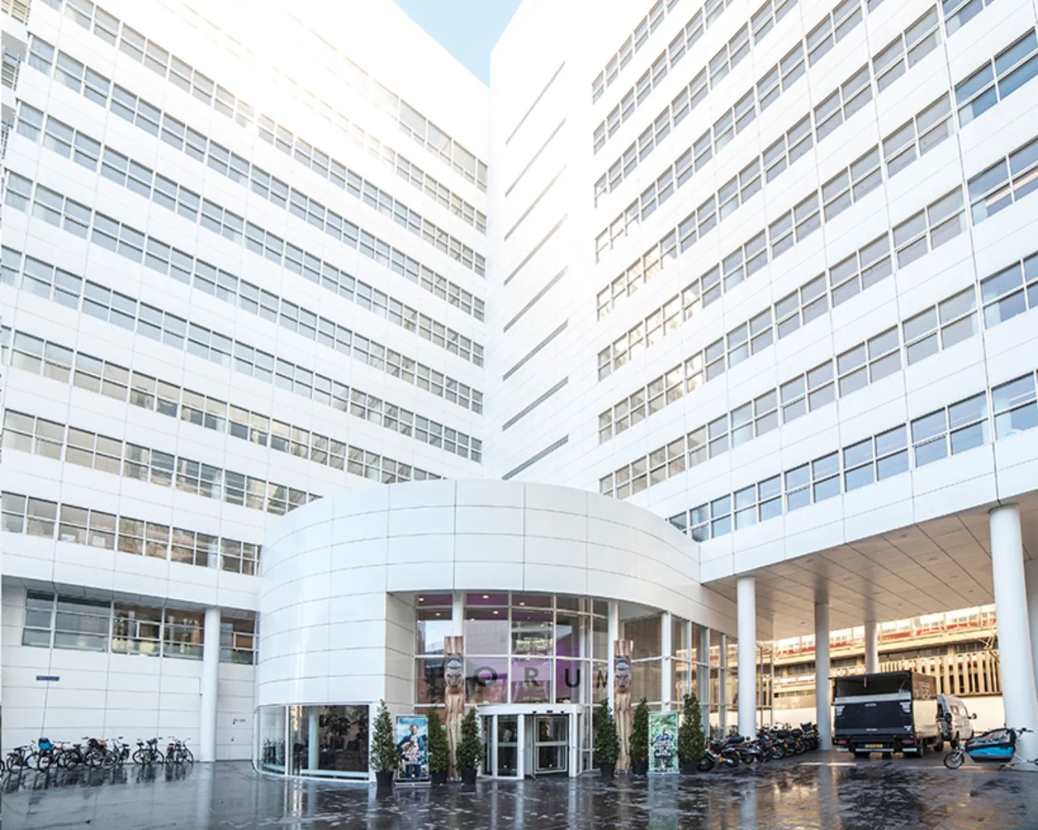 Ingang van een modern wit kantoorgebouw met grote ramen en een glazen entree, genaamd Forum.