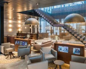 Stijlvol ingerichte hotellounge met moderne fauteuils, houten accenten, een boekentafel en een zwevende trap.