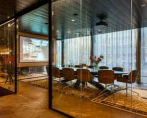 Moderne vergaderruimte met glazen wanden, een grote tafel, leren stoelen en een projector met scherm.