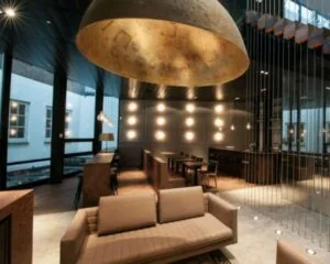 Modern ingerichte lounge met warme verlichting, hoge plafonds en een opvallende gouden hanglamp.