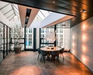 Modern vergaderruimte met ronde houten tafel, designstoelen, opvallende hanglamp en glazen dak.