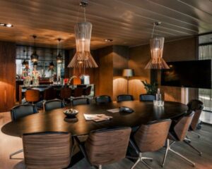Moderne vergaderruimte met een grote ovale tafel, houten stoelen, designverlichting en een flatscreen aan de muur.