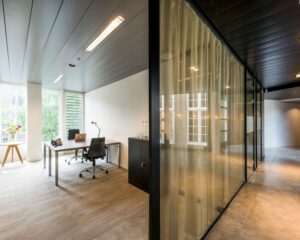 Modern ingericht kantoor met een bureau, bureaustoel en glazen wand met gordijn.