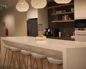 Moderne kantoorkeuken met een wit kookeiland, barkrukken, hanglampen en een fruitschaal.