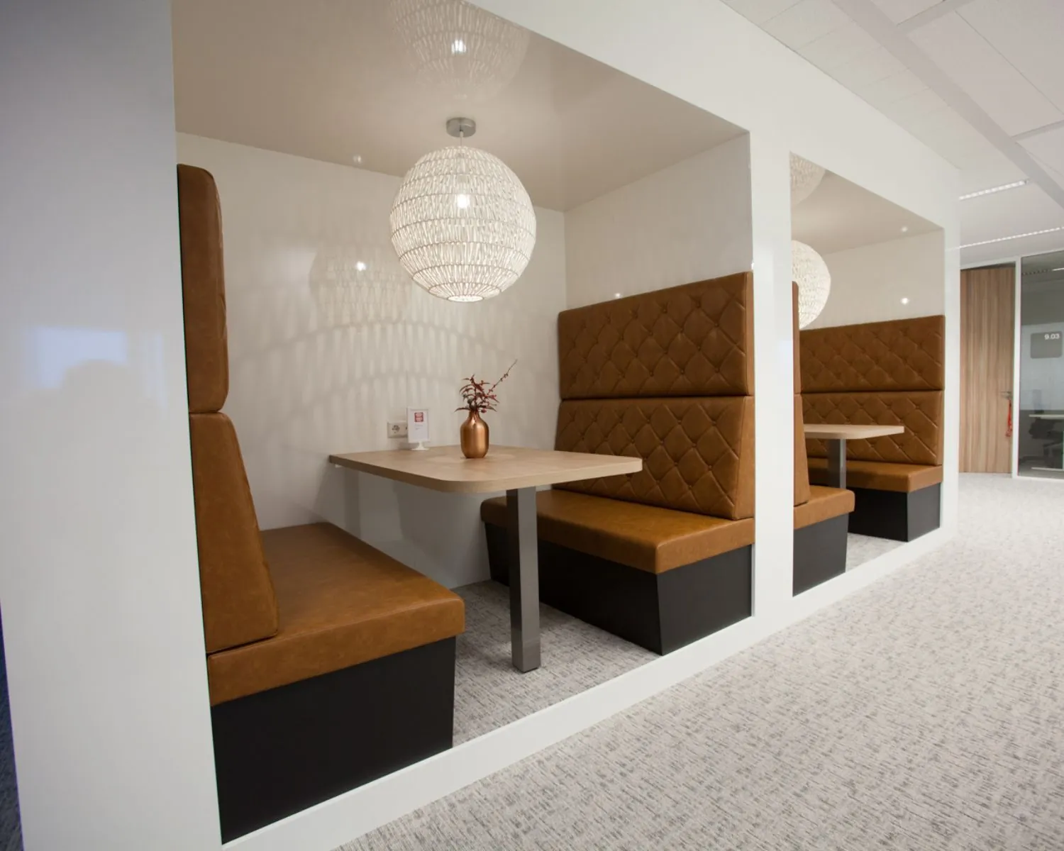Moderne kantoorruimte met ingebouwde zitnissen, bekleed met bruine leren kussens en ingericht met houten tafels en decoratieve hanglampen.