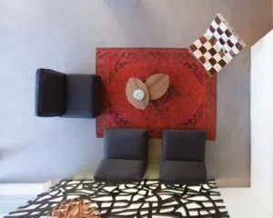 Moderne zithoek van bovenaf gezien met een rood Perzisch tapijt, zwarte zitstoelen, een houten salontafel en een geblokte designstoel.