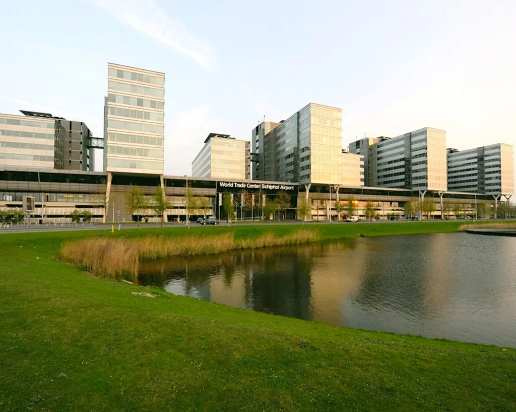 Het World Trade Center Schiphol Airport met moderne kantoorgebouwen, gezien vanaf een vijver met grasveld op de voorgrond.