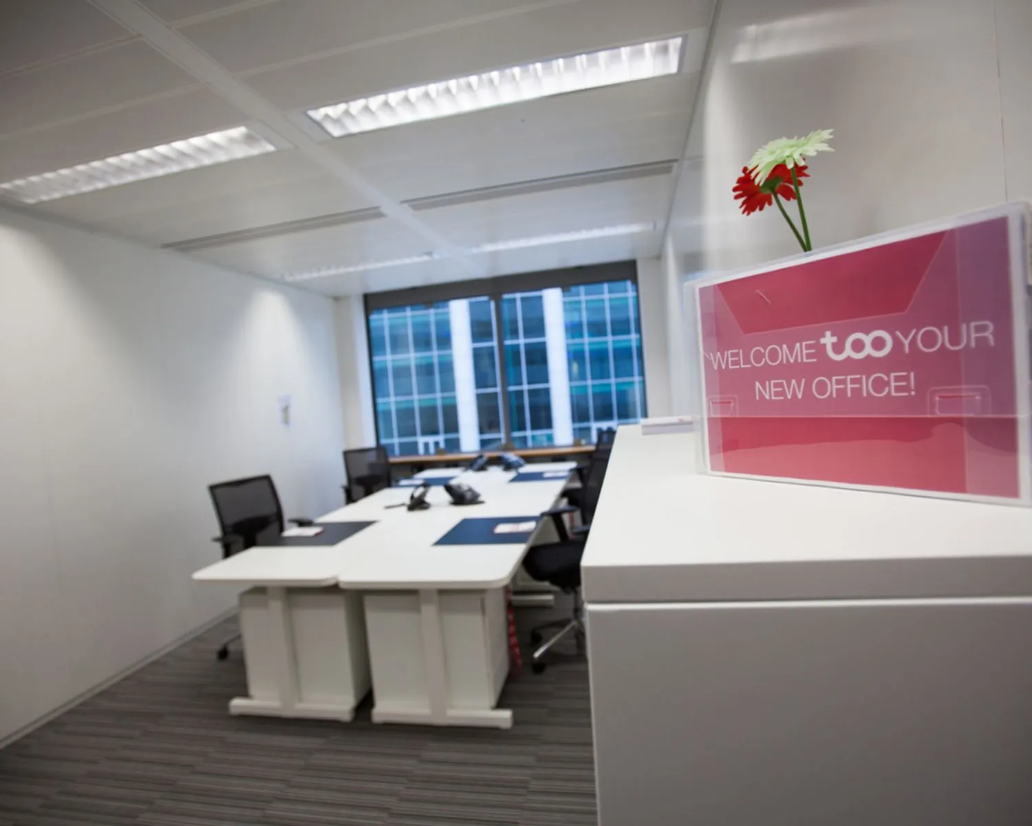 Moderne kantoorkamer met vier bureaus en een bord met de tekst "Welcome to your new office!".