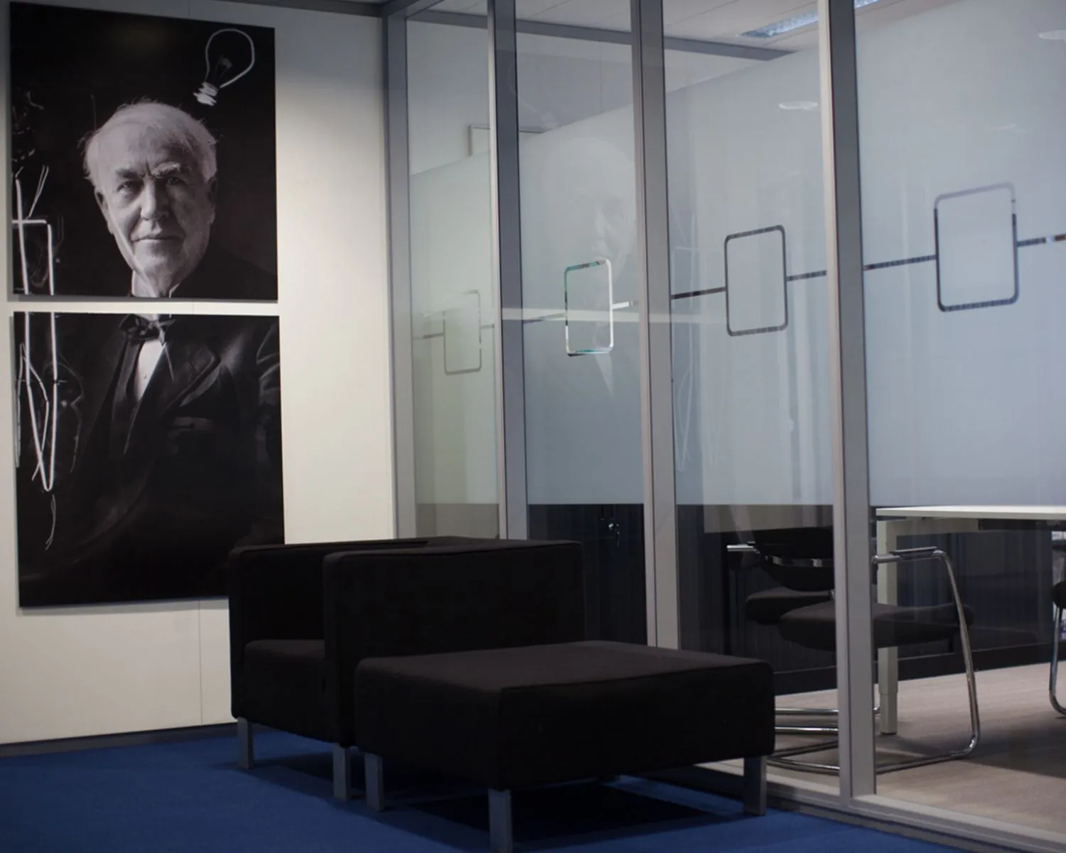 Zwarte fauteuils in een moderne kantoorruimte met een grote zwart-witfoto van Thomas Edison aan de muur.