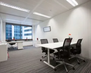 Modern ingericht kantoor met een vergadertafel, bureaus en grote raamkozijnen met uitzicht op een kantoorgebouw.