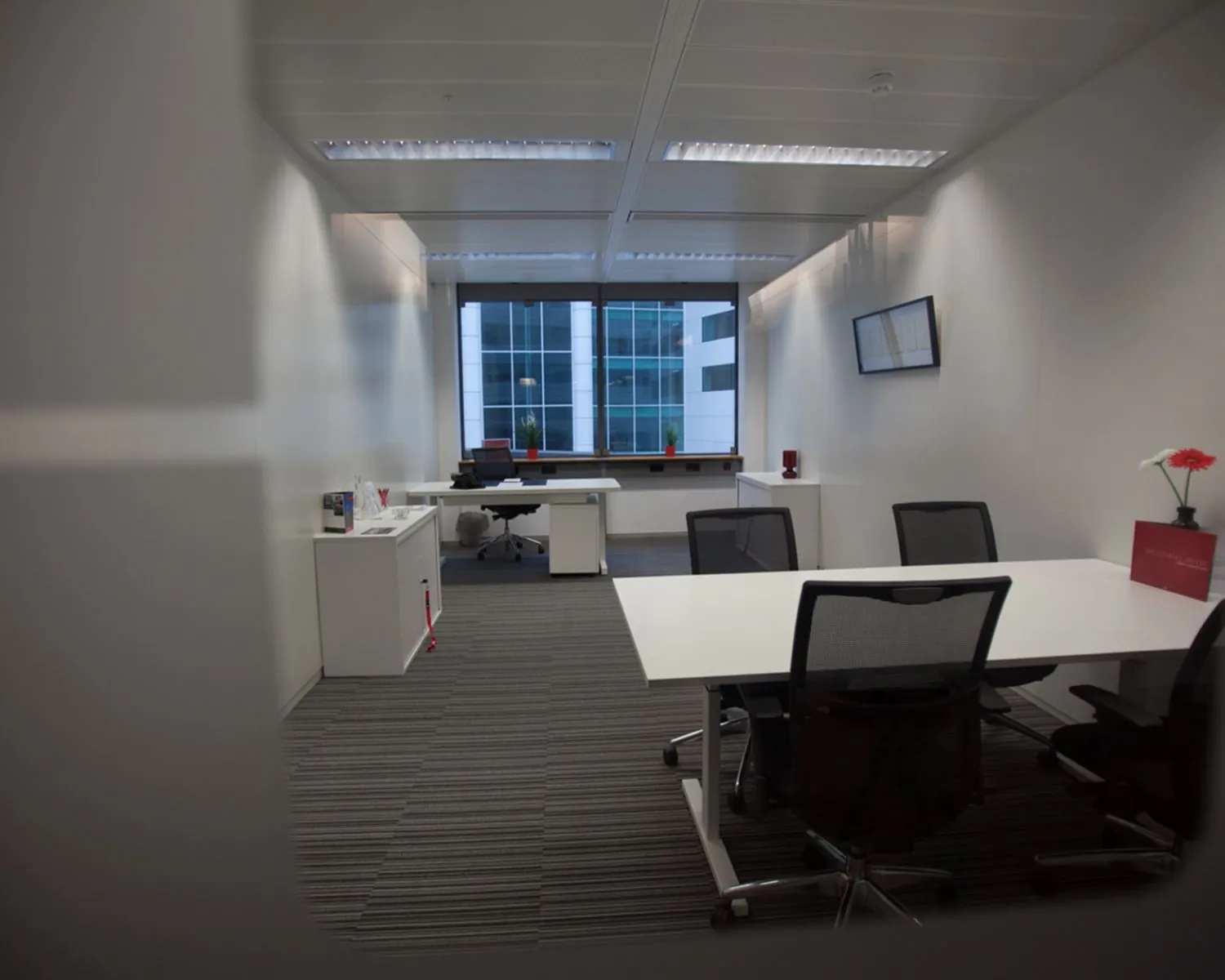 Moderne kantoorkamer met vergadertafel, bureaustoel, en groot raam met uitzicht op een kantoorgebouw.