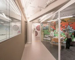 Twee mannen spelen tafelvoetbal in een moderne kantoorruimte met kleurrijke muurschilderingen en glazen wanden.