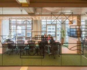 Een vergaderruimte met glazen wanden waarin mensen samenwerken rond een tafel in een modern kantoor met uitzicht op een stad.