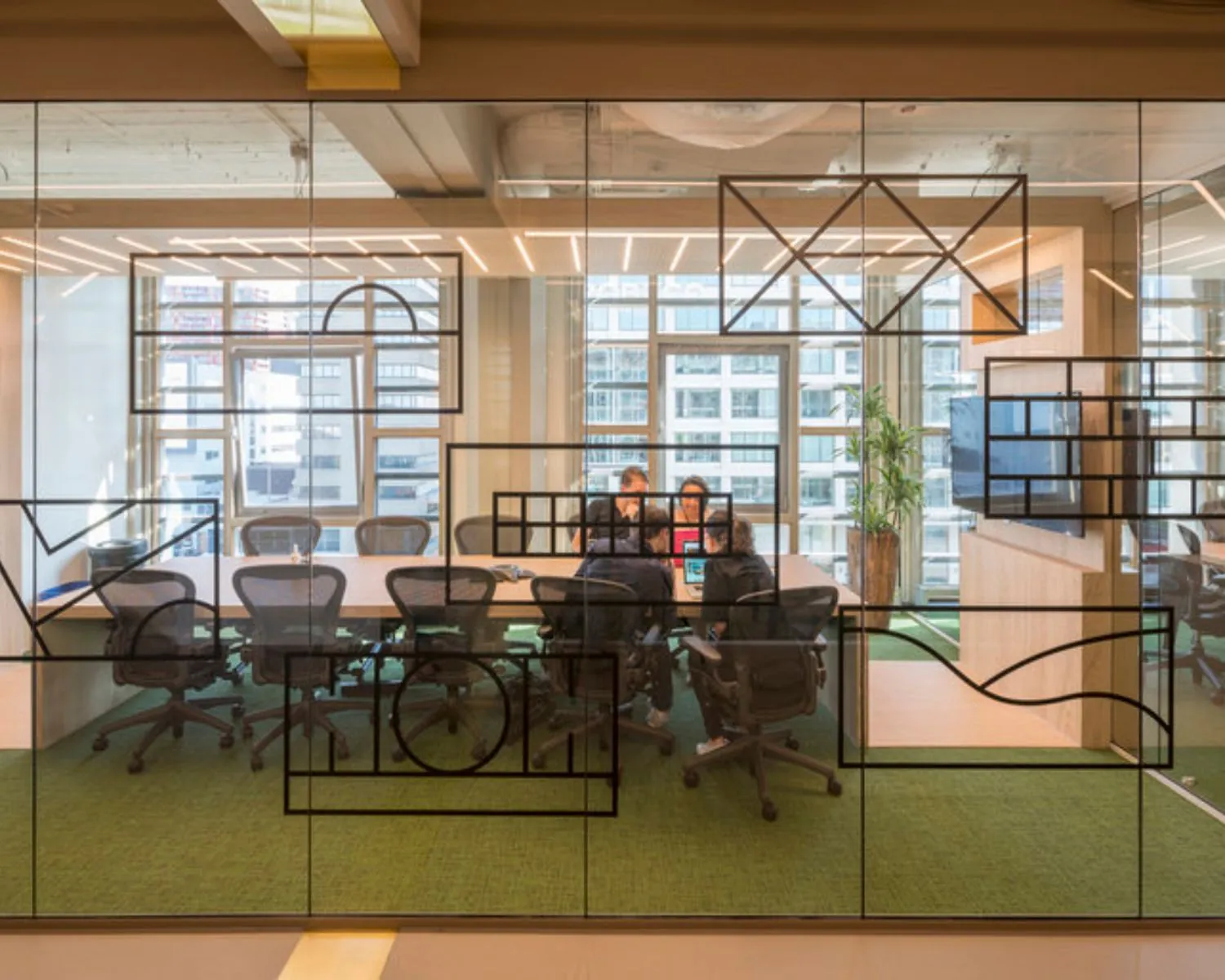 Een vergaderruimte met glazen wanden waarin mensen samenwerken rond een tafel in een modern kantoor met uitzicht op een stad.