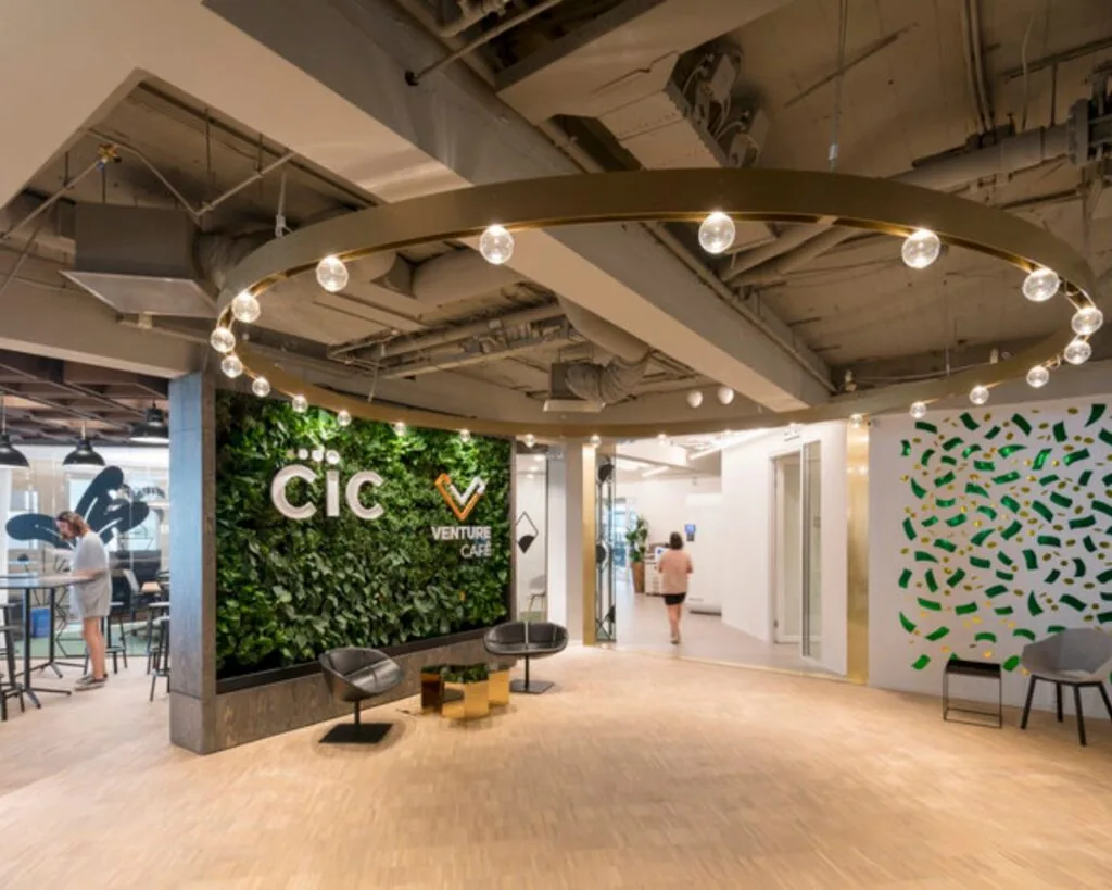 Moderne kantoorlobby van CIC Venture Café met een groene plantenwand, zitgelegenheid en designverlichting.