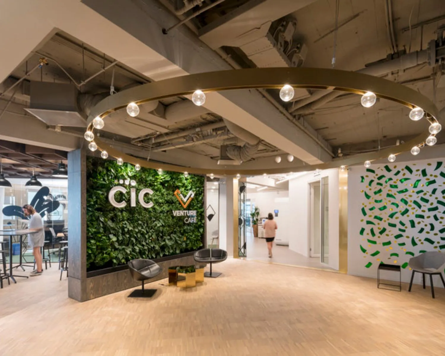 Moderne kantoorlobby van CIC Venture Café met een groene plantenwand, zitgelegenheid en designverlichting.