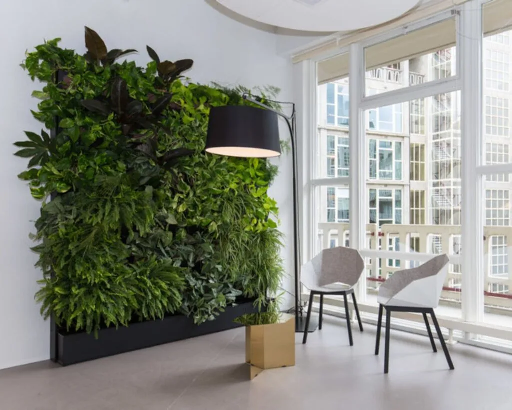 Moderne zithoek met twee stoelen en een ronde tafel bij een grote raamwand, naast een groene verticale plantenmuur.