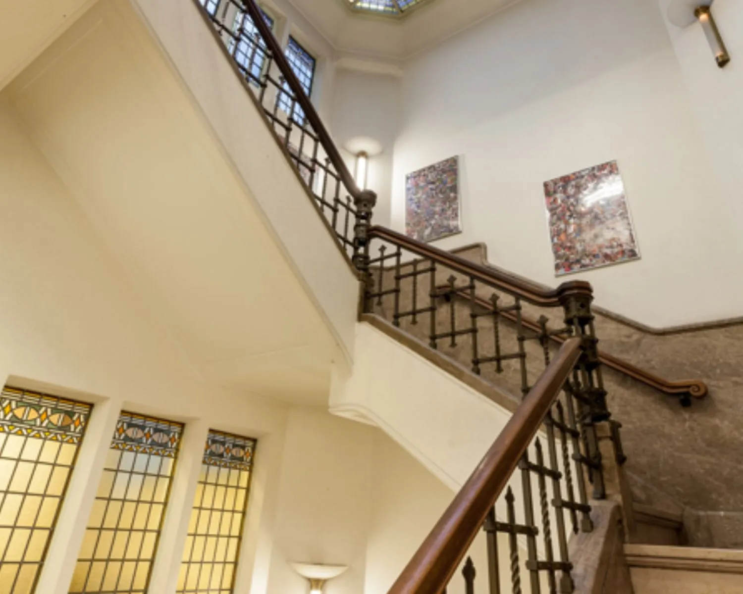 Monumentaal trappenhuis met een klassieke houten leuning, glas-in-loodramen en moderne kunst aan de muur.