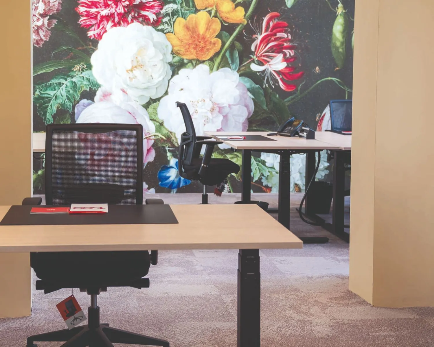 Moderne kantoorruimte met bureaus en bureaustoelen, tegen een kleurrijke bloemenmuur als achtergrond.