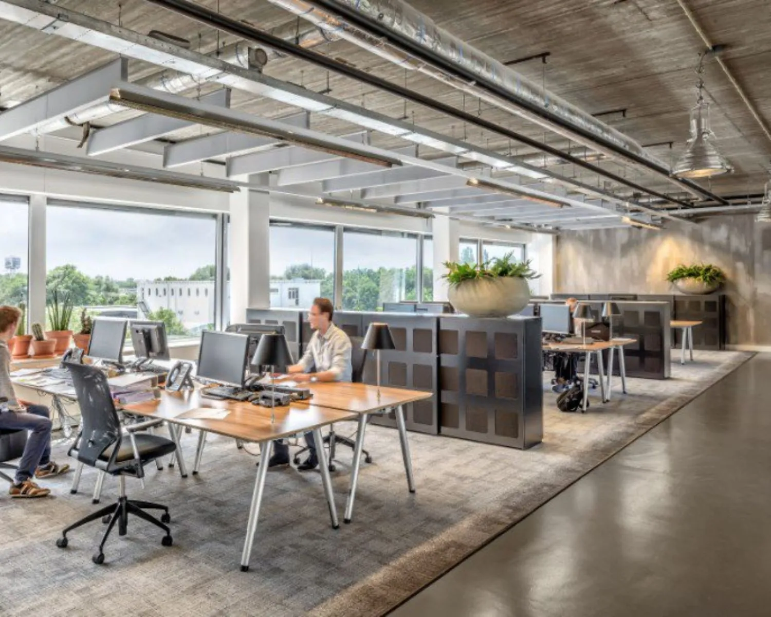 Moderne open kantoortuin met bureau-eilanden, grote ramen en veel natuurlijk licht.