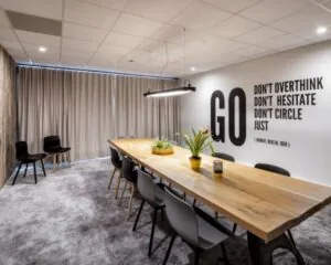 Vergaderruimte met een lange houten tafel, moderne stoelen, kamerplanten en een motiverende quote op de muur.