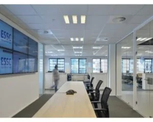 Vergaderruimte met glazen wanden, meerdere bureaustoelen en beeldschermen met het logo van ESSC.