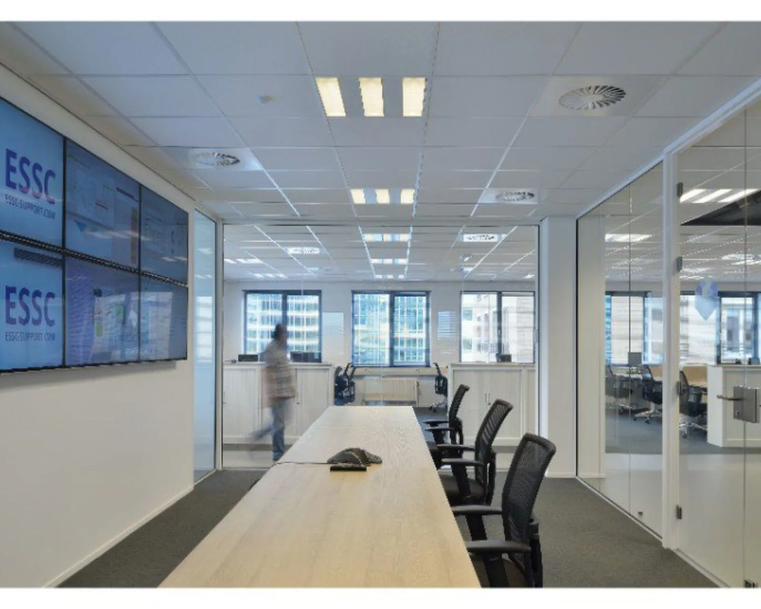 Vergaderruimte met glazen wanden, meerdere bureaustoelen en beeldschermen met het logo van ESSC.