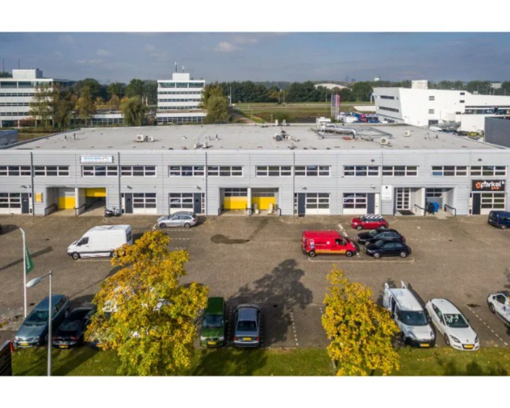Bedrijfsverzamelgebouw met parkeerplaatsen ervoor, gezien vanuit de lucht op een zonnige dag.