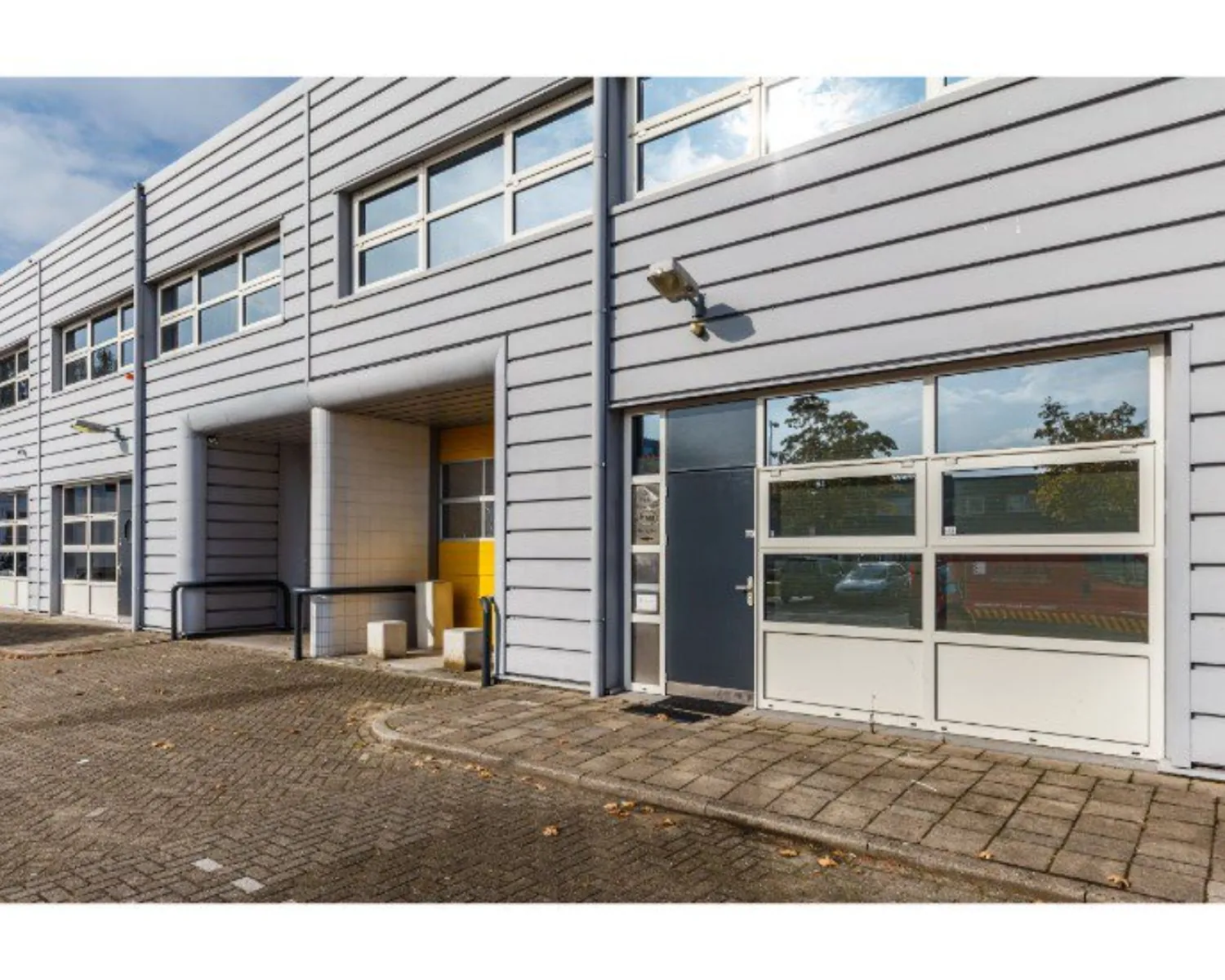 Grijze bedrijfsunits met glazen garagedeuren en gele accenten aan de buitenzijde.