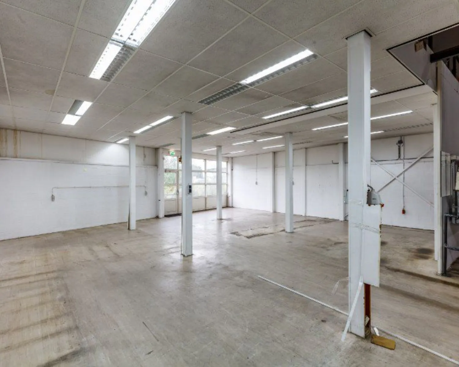 Leegstaand industrieel magazijn met betonnen vloer, witte muren en meerdere steunpilaren.