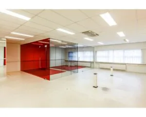 Lichte, lege kantoorruimte met een glazen vergaderruimte met rode wanden in het midden.