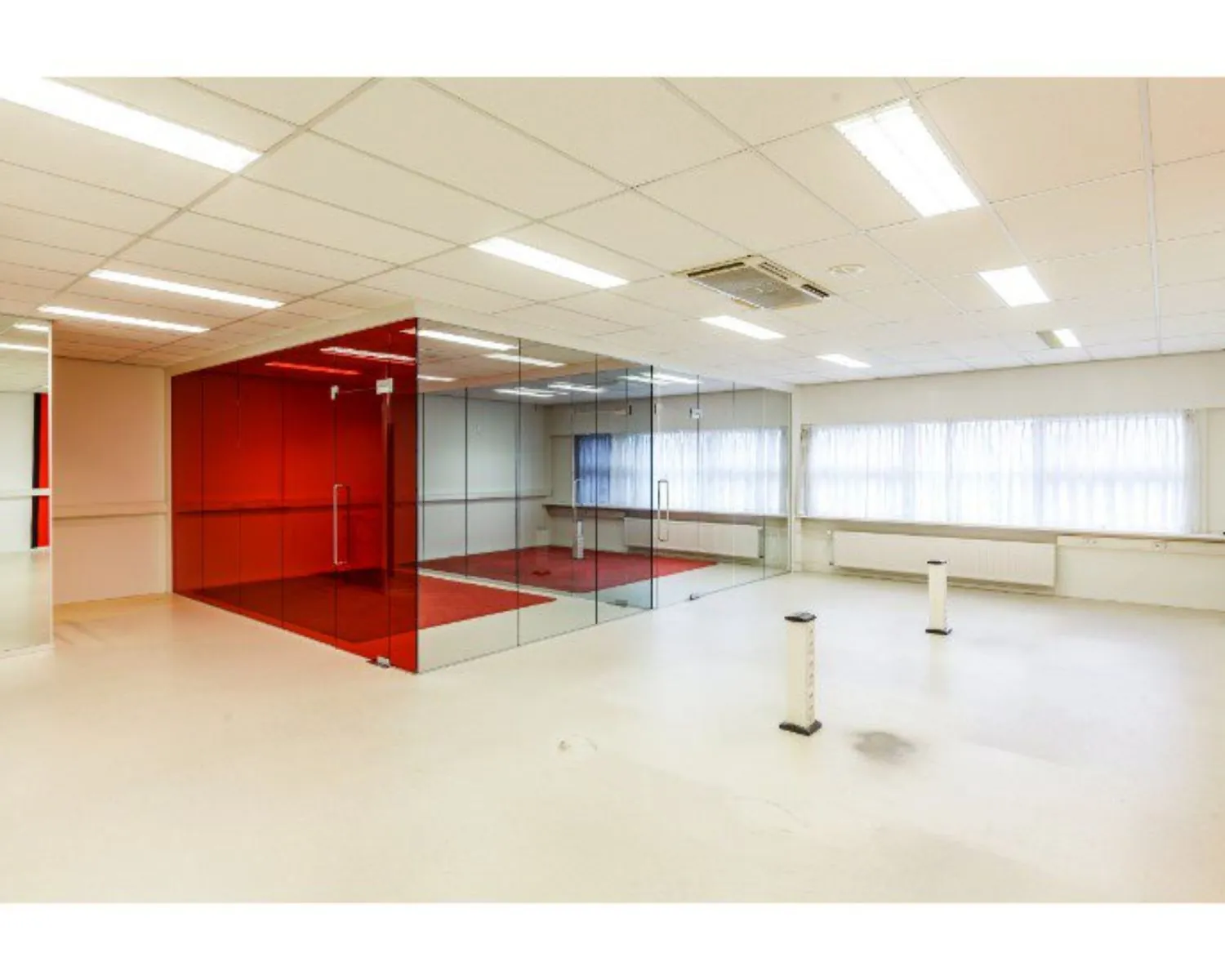 Lichte, lege kantoorruimte met een glazen vergaderruimte met rode wanden in het midden.