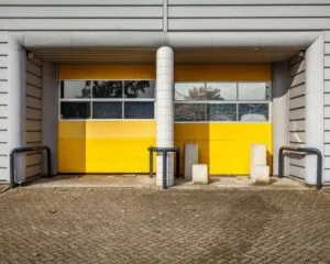 Twee gesloten gele roldeuren van een industrieel gebouw met grijze gevelbekleding en beschermbeugels.