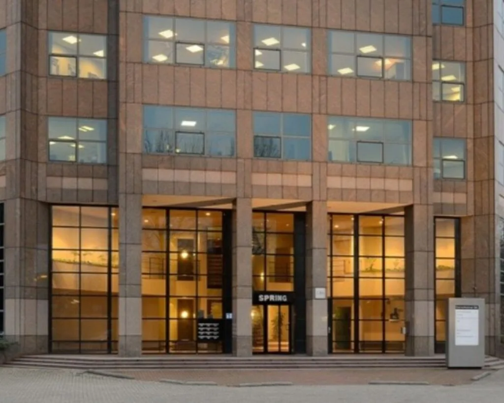 Vooraanzicht van een modern kantoorgebouw met grote ramen en de naam 'SPRING' boven de entree.
