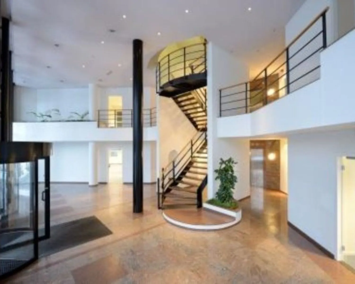 Moderne, open kantoorentree met een wenteltrap, glazen draaideur en strakke afwerking.
