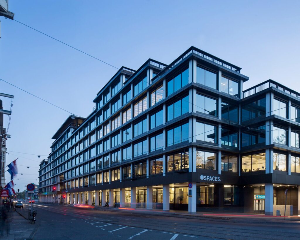 Modern kantoorgebouw van Spaces met glazen gevel aan een stadsstraat bij schemering.
