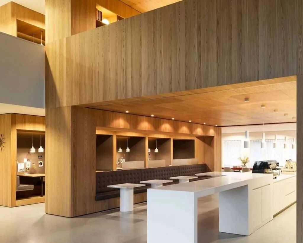 Modern ingerichte kantine met houten wanden, ingebouwde zitnissen en een wit kookeiland met koffiezetapparaat.