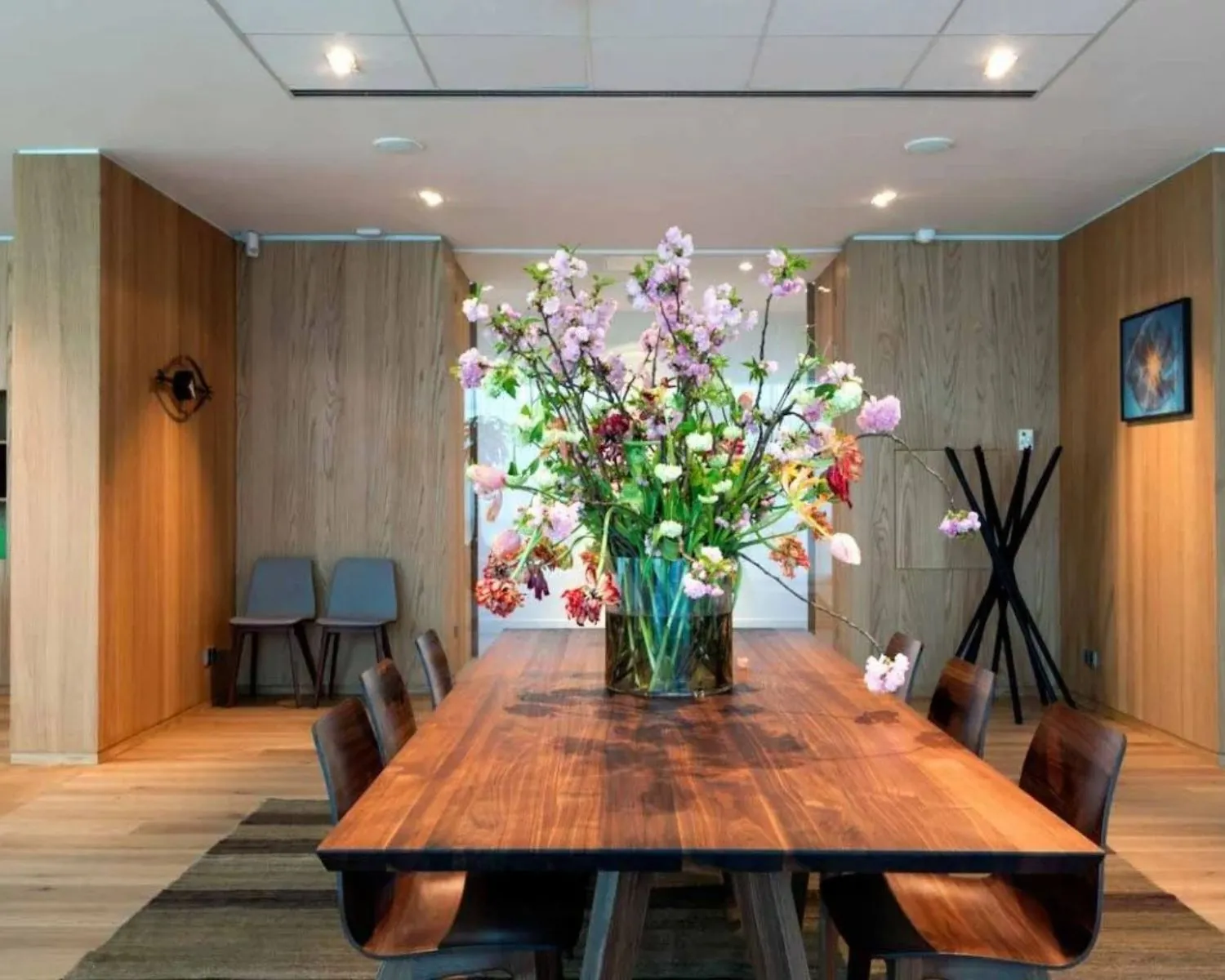 Houten vergadertafel met een grote vaas kleurrijke bloemen in een modern ingerichte ruimte.