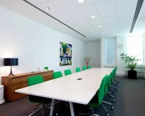Moderne vergaderruimte met een lange witte tafel, groene stoelen en kleurrijk schilderij aan de muur.